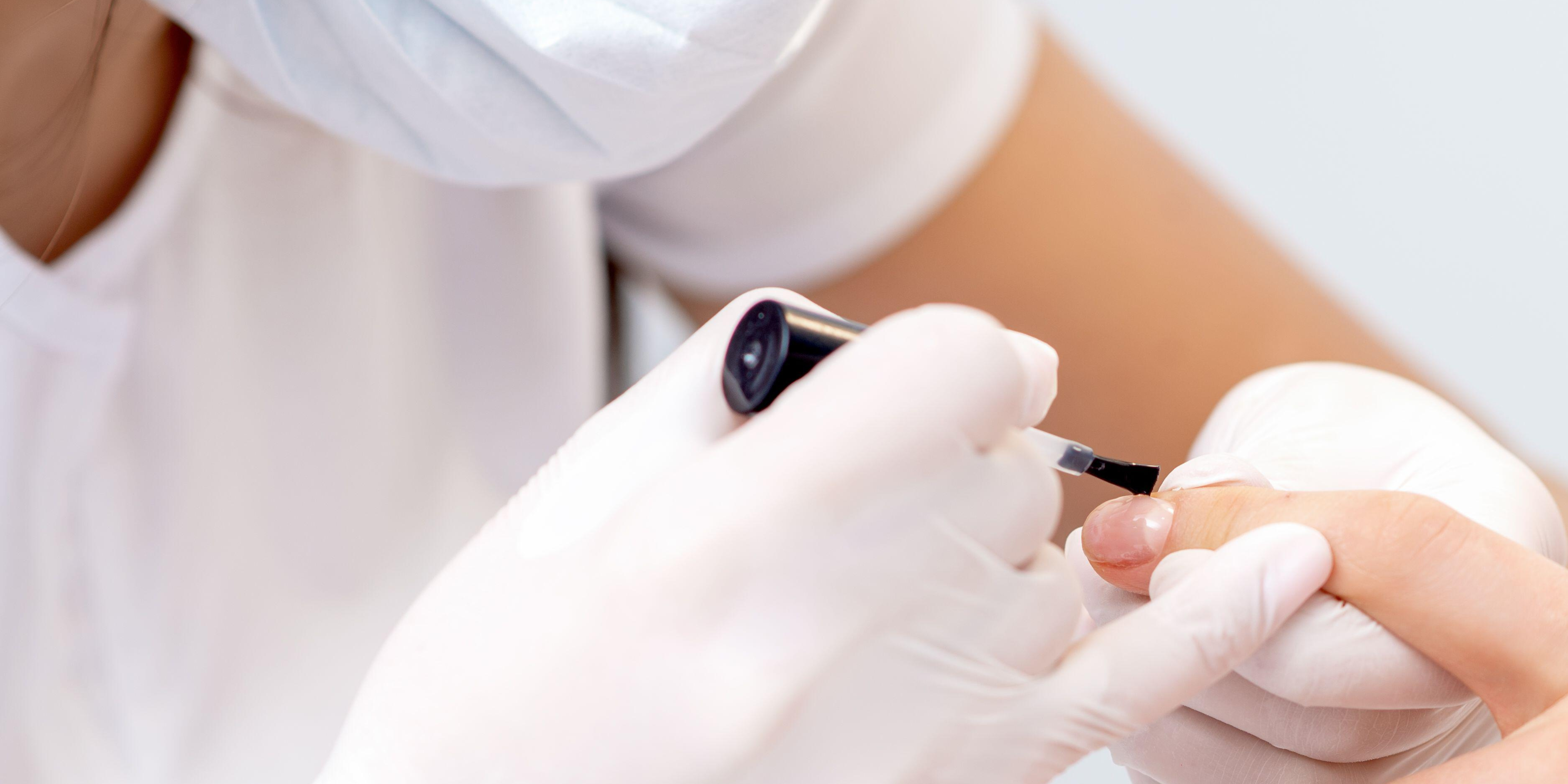 A picture of a nail technician applying nail polish to someone's fingernails